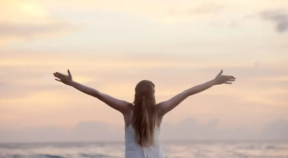 optimiz: bien-être mental. Personne de dos, bras ouverts face à un ciel doux au coucher du soleil, symbole de respiration et lâcher-prise