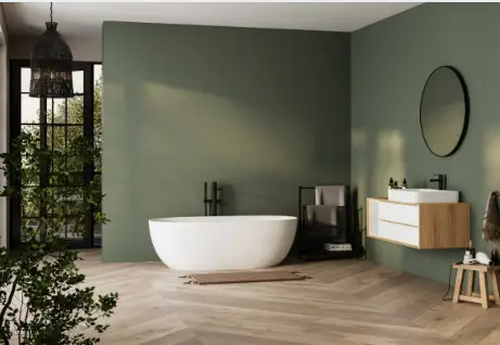 Salle de bain moderne avec mur vert, baignoire îlot blanche, meuble vasque bois suspendu, miroir rond, robinetterie noire et parquet à chevrons